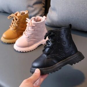 Bottines en similicuir à lacets, dans ses trois couleurs et posées sur un canapé gris. On voit au premier plan une main qui tient une bottine noire.