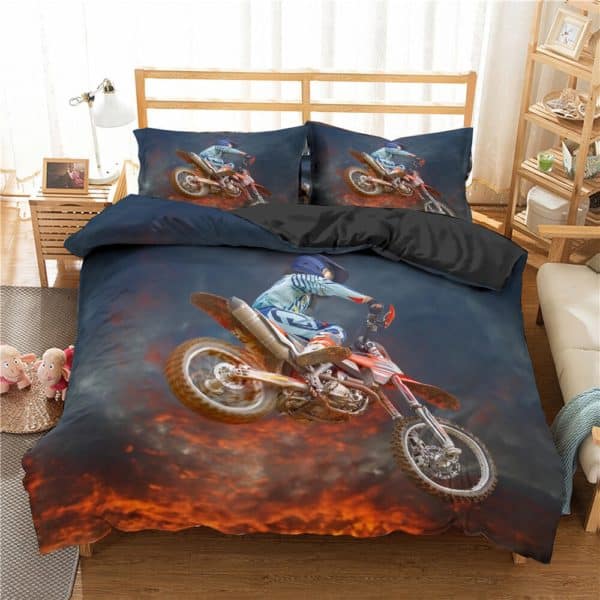 Dans une chambre d'enfant , est installée sur le lit une parure complète dans les tons sombres sur laquelle il y a une image d'une motocross en plein saut où on voit le coucher de soleil se refléter sur les nuages sombres