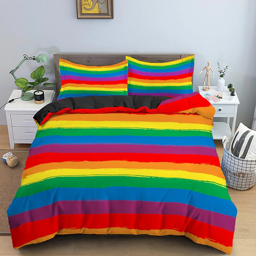 Dans une chambre un lit, avec table de chevet de chaque coté, est couvert d'une parure complete de lit recouverte entièrement de bandes de couleurs créant un arc en ciel