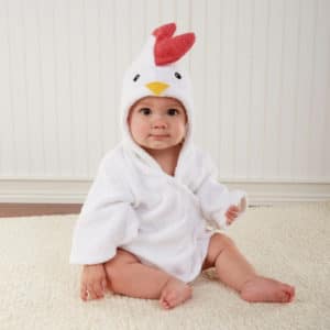Petit bébé installé assis et qui porte un peignoir de bain blanc dont la capuche représente une tête de coq avec une crête rouge, ,deux yeux et un petit bec orange