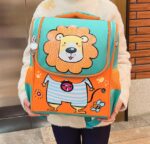 Cartable garçon lion ou dino tenu dans les mains d'un enfant dont on ne voit pas le visage