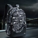 Sac à dos garçon cm2 noir avec motifs blanc dessinés présenté sur fond urbain de nuit