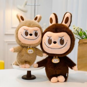 2 peluches style Labubu, une moyenne posée sur un présentoir à gateau de couleur marron clair, et une autre plus grosse marron foncé, posé à coté directement sur la table.