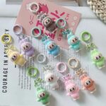 Plusieurs petits porte-clés peluches représentants un personnage rigolo avec oreilles de lapin, style monstre Labubu, de couleurs différentes pastels, sur un magasine
