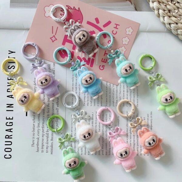 Plusieurs petits porte-clés peluches représentants un personnage rigolo avec oreilles de lapin, style monstre Labubu, de couleurs différentes pastels, sur un magasine