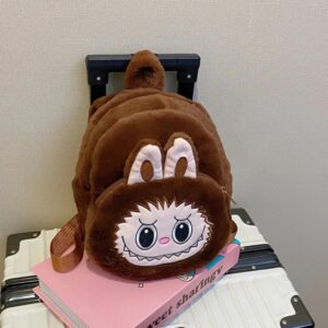 sac à dos marron en peluche, avec oreilles de lapin et visage rigolo cousu, sur le sommet d'une valise blanc et noir .