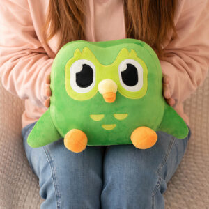 Peluche Duo, issu de l'univers Duolingo, petite mascotte verte à l'image d'un hibou espiègle assis et tenu par une jeune fille.