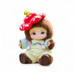 Peluche Wakuku officielle - Gentleman flower, un visage d'enfant espiègle au trait Kawaii, en peluche marron, vêtu d'une salopette jaune pastel, d'un nœud papillon et d'un chapeau en forme de fleur rouge à pois blanc sur fond blanc.