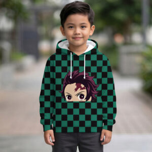 Un petit garçon souriant portant un sweat Demon Slayer Tanjiro à carreaux verts et noirs avec le visage du héros imprimé, posant debout dans une allée extérieure avec des plantes en arrière-plan.