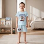 Un jeune garçon porte un pyjama court Demon Slayer Inosuke bleu clair avec un dessin d’Inosuke, dans une chambre lumineuse avec un lit et des jouets en arrière-plan.