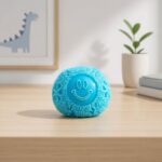 Un jouet anti-stress sensoriel Needoh en forme de boule à picots bleue, posé sur une table en bois dans une chambre avec une plante et un dessin de dinosaure.