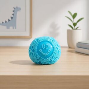Un jouet anti-stress sensoriel Needoh en forme de boule à picots bleue, posé sur une table en bois dans une chambre avec une plante et un dessin de dinosaure.
