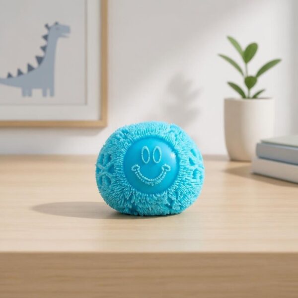 Un jouet anti-stress sensoriel Needoh en forme de boule à picots bleue, posé sur une table en bois dans une chambre avec une plante et un dessin de dinosaure.