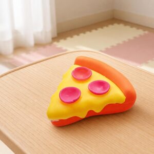 Un jouet anti-stress sensoriel Needoh en forme de pizza posé sur une table en bois, avec une part jaune et orange et trois rondelles roses.