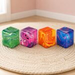 Quatre cubes anti-stress colorés avec effet marbré, posés sur un tapis rond dans une pièce lumineuse : le lot de 4 jouets anti-stress sensoriels Needoh en cubes marbrés.