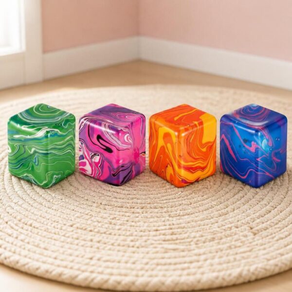 Quatre cubes anti-stress colorés avec effet marbré, posés sur un tapis rond dans une pièce lumineuse : le lot de 4 jouets anti-stress sensoriels Needoh en cubes marbrés.