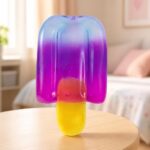 Un Jouet anti-stress sensoriel Needoh glace à l'eau squishy en forme de glace colorée, posé sur une table dans une chambre lumineuse.