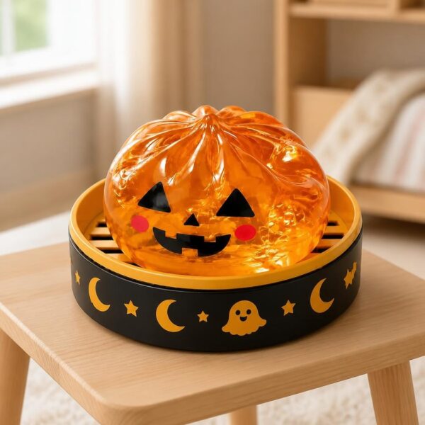 Un jouet garçon anti-stress Halloween citrouille qui sourit, en forme de petite citrouille orange avec un visage rigolo, posé dans un bol noir décoré d’Halloween sur une table en bois.