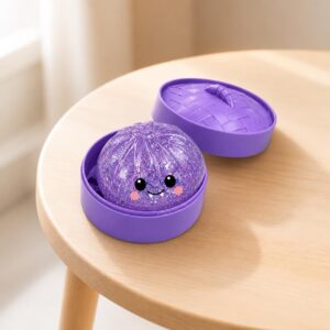 Un jouet garçon anti-stress Halloween violet plein de paillettes en forme de petite balle souriante, posé dans une boîte violette ouverte sur une table en bois clair.