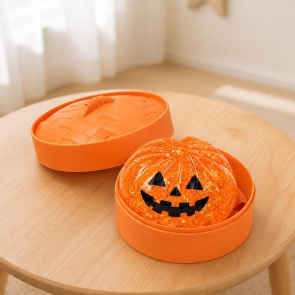 Un jouet garçon anti-stress Halloween vraie tête de citrouille orange, posé dans une boîte ronde, sur une petite table en bois dans une pièce lumineuse.