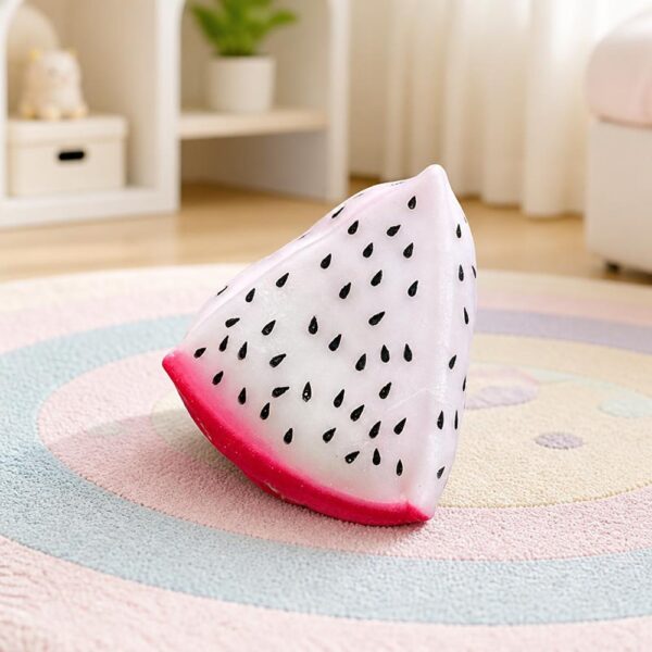 Un Jouet Squishy garçon en quartier de fruit du dragon blanc et rose, posé sur un tapis rond dans une chambre lumineuse.