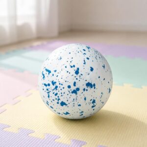 Un jouet Squishy Needoh garçon anti-stress en balle mouchetée, une boule blanche avec des taches bleues, posée sur un tapis coloré en mousse.