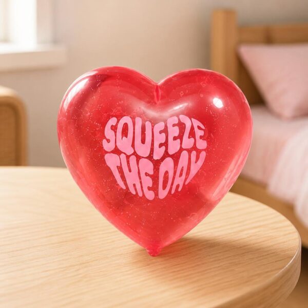 Un jouet Squishy Needoh garçon anti-stress en cœur translucide rouge posé sur une table, dans une chambre douce et lumineuse.