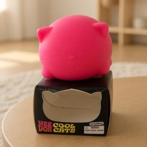 Un jouet squishy Needoh garçon anti-stress en chaton à presser rose posé sur sa boîte, dans une pièce lumineuse.