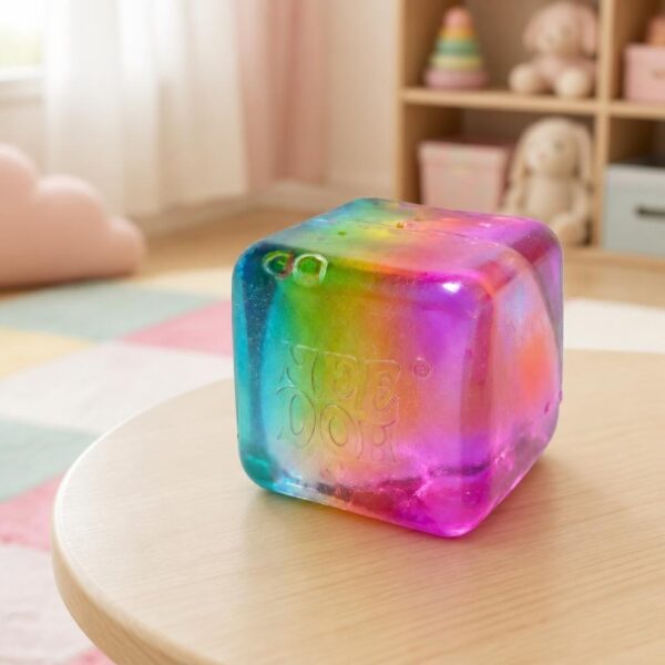 Un Jouet Squishy Needoh garçon anti-stress en cube dégradé multicolore posé sur une petite table dans une chambre d’enfant.