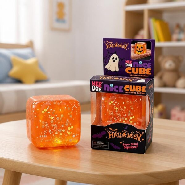 Un Jouet Squishy Needoh garçon anti-stress en cube Halloween orange posé sur une table, avec sa boîte violette Halloween et une lumière qui brille à l’intérieur.