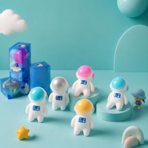 Des figurines d’astronautes colorées représentant le squishy garçon anti-stress en forme de cosmonaute 2 pièces aléatoires, présentées devant leurs boîtes bleues sur un décor turquoise.
