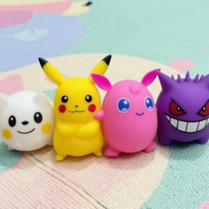 Un lot de quatre squishies représentant des personnages Pokémon colorés, dont Pikachu, Rondoudou et Ectoplasma, posé sur un tapis aux motifs pastel.