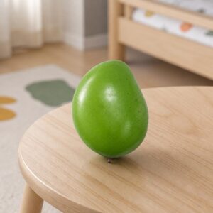 Un squishy garçon mangue réaliste sensible à la chaleur, en forme de mangue verte, posé sur une table ronde en bois dans une pièce lumineuse.
