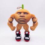 Une peluche Italian Brainrot Gigachad Muscle-Tung représentant un personnage musclé orange avec un visage humain, des chaussures noires et rouges, sur un fond blanc.